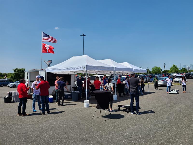 Canopies and trailer in a sunny ballpark lot with a team flag flying