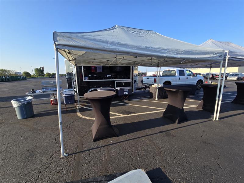Bar-height cocktail tables under a canopy beside the trailer