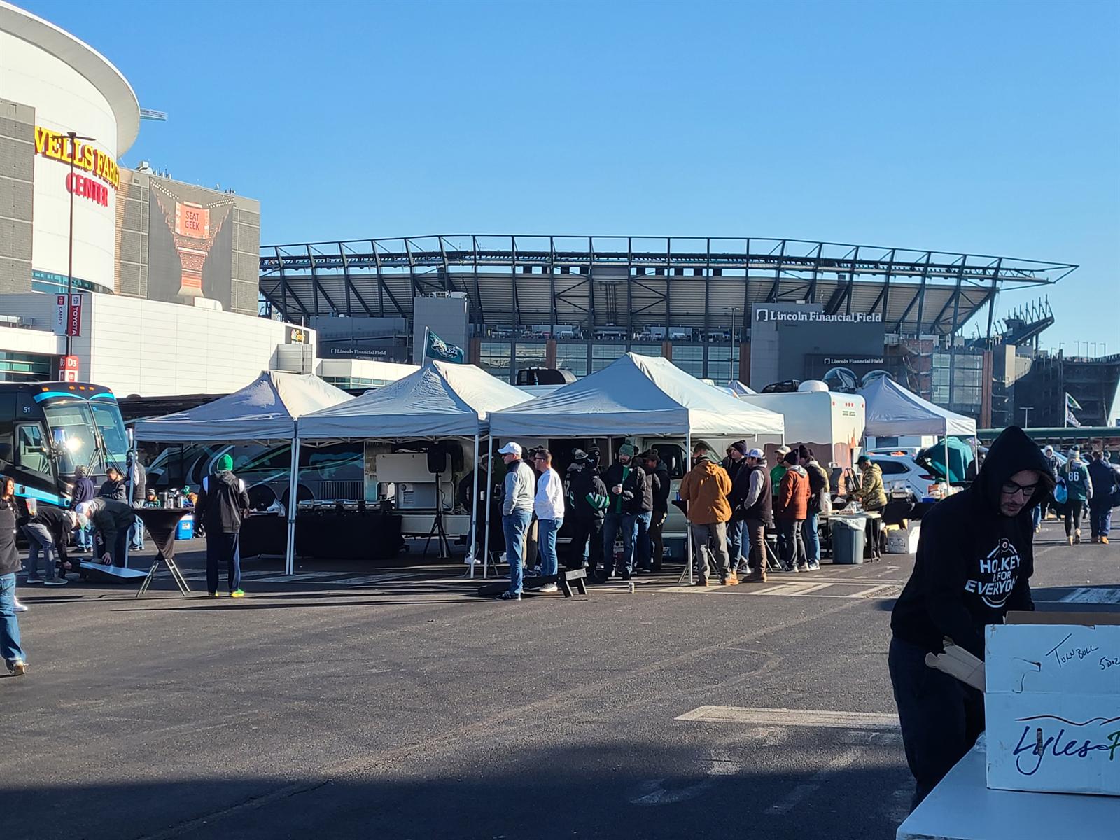 Fans in green gathered under white canopies in front of a football stadium