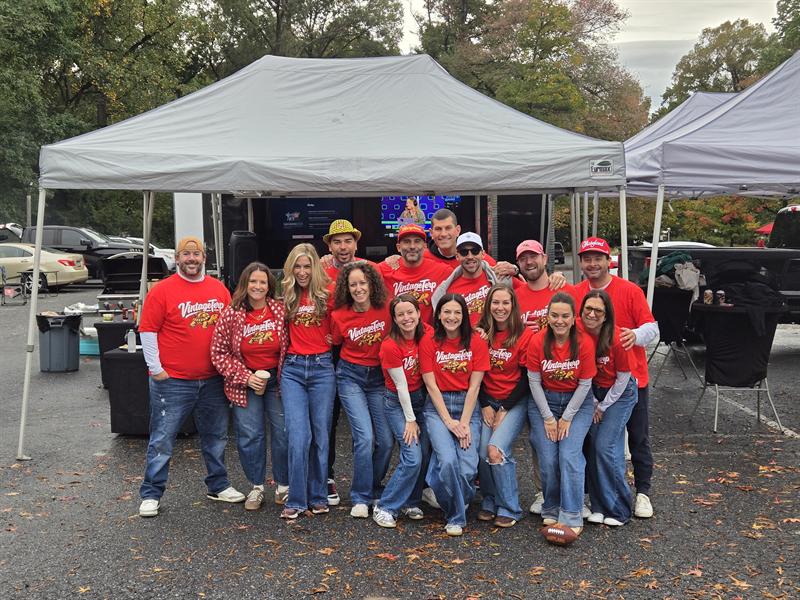 Company group in matching red shirts posing under a canopy