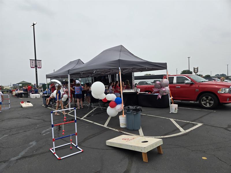Ladder toss and cornhole games set up beside a tent with red, white and blue balloons