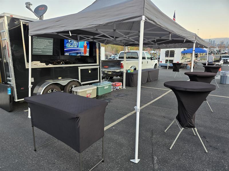 Tailgate trailer with a TV, canopy, draped table and bar-height cocktail tables set up before guests arrive
